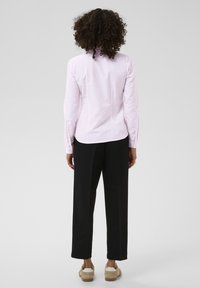 Chemise rose clair à manches longues avec des rayures blanches, associée à un pantalon large noir et des chaussures beige avec des accents blancs.