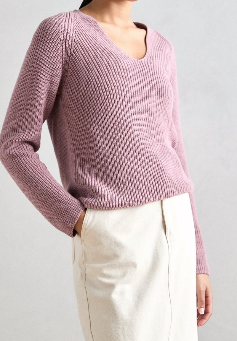 Maglione a coste di colore rosa chiaro con scollo a V e maniche lunghe, abbinato a una gonne di colore crema in un tessuto leggermente strutturato.