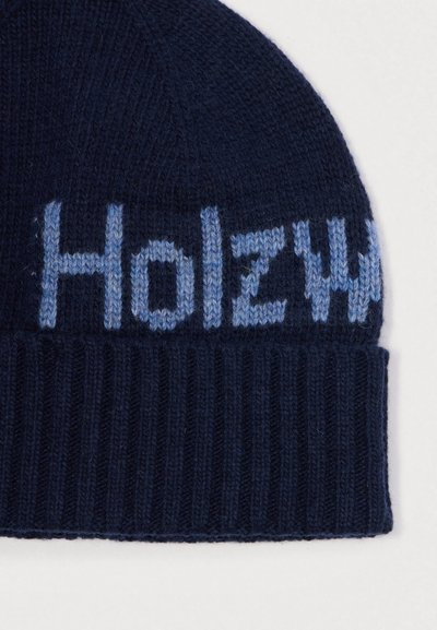 Pletená čiapka v tmavomodrej farbe s svetlomodrým textom "Holz". Má ryhovanú textúru a priliehavý strih. Vyrobená z mäkkého a teplého materiálu.