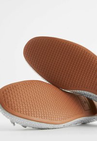 Graue Sportschuhe mit strukturierten Gummisohlen. Die Sohlen verfügen über einen braunen, gemusterten Griff für besseren Halt. Leichte Strick-Oberteile sind sichtbar.