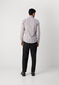 Μπλούζα με μακρύ μανίκι σε λευκό φόντο και πολύχρωμο λουλουδάτο σχέδιο, συνδυασμένη με μαύρο παντελόνι και μαύρα παπούτσια.