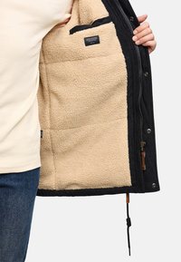 Zwarte corduroyjas met een tan fleece voering, voorzien van een ritsluiting, drukknoopsluiting en een zak in de binnenvoering.