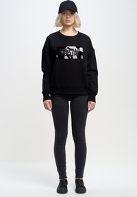 Černá mikina s oversized střihem, zdobená lesklým logem "BIG STAR". Kombinováno s černými skinny džíny a černými teniskami. Bílá pozadí.