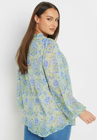 Blusa floreale a maniche lunghe, con un motivo blu chiaro, verde e giallo su tessuto trasparente, col collo rotondo e vestibilità rilassata.