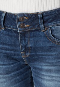 Jean en denim avec un lavage bleu foncé, doté de deux boutons en métal à la taille, de coutures orange et d'un léger délavage sur le tissu.
