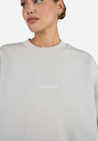 Light gray sweatshirt with a ribbed neckline and oversized fit. Features embroidered "PEGADOR" logo in white on the front.
