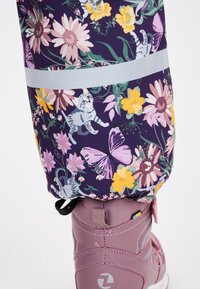Floral regenbroek in donkerpaars met kleurrijke bloemen, vlinders en katten. Bevat een reflecterende strip en een aangesloten manchette over een roze laars.