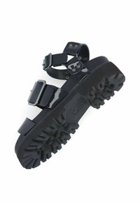 Sandales noires brillantes avec une semelle épaisse et robuste, des sangles ajustables et de grosses boucles ; conçues pour la durabilité et l'adhérence.