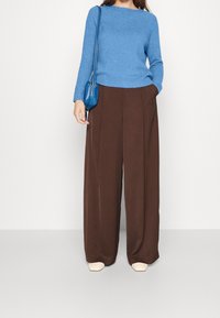 Maglione lavorato a maglia di colore azzurro chiaro, pantaloni a gamba larga marroni e scarpe beige. Le caratteristiche includono una trama a coste e tasche laterali sui pantaloni.