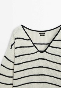 Pull rayé crème et marine, avec un col en V, une texture tricotée et un subtil bord côtelé. Fabriqué en coton.