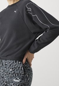 Felpa nera con logo Puma grigio sulla manica sinistra, abbinata a pantaloni jogger grigi con stampa leopardata e logo Puma bianco sul davanti.