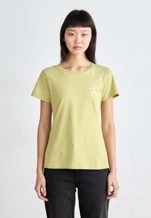 T-shirt en coton vert clair à manches courtes, col rond, avec un petit logo blanc sur la poitrine gauche. Associé à un jean foncé.