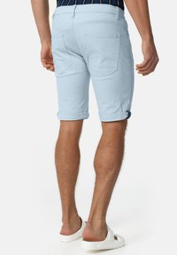 Svijetloplave kratke hlače koje se mogu rolati s uskim krojem, izrađene od mekanog materijala. Imaju dva stražnja džepa i srednji struk, uparene s bijelim sandalama.