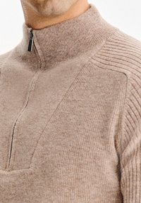 Beżowy półsuwny polar z textured knit, z prążkowanym kołnierzem i panelami bocznymi oraz gładkimi sekcjami z przodu.