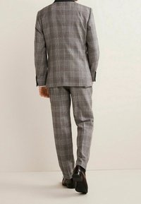 Abito a quadri grigio composto da giacca su misura e pantaloni coordinati. Il tessuto presenta un motivo a scacchi con sottili accenti rossi e una consistenza liscia.