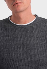 Grau strukturierter Strickpullover mit rundem Ausschnitt, der einen kontrastierenden weißen Innenkragen aufweist. Nahaufnahme des Stoffmusters und der Details.