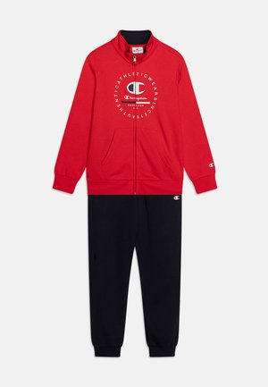 Giacca rossa con zip e logo bianco sul petto, abbinata a pantaloni tuta blu scuro, entrambi realizzati in morbido tessuto spazzolato.