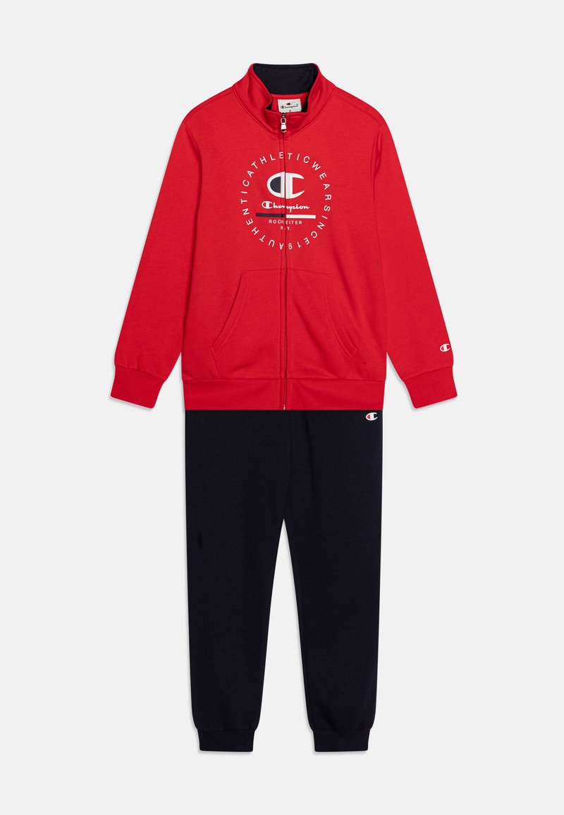Chaqueta roja con cremallera y logo blanco en el pecho, combinada con pantalones de chándal azul marino, ambos hechos de un suave tejido cepillado.