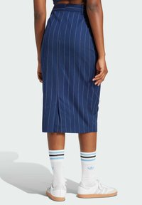 Marinblå pennkjol med vertikala ränder, med en slits bak. Kompositmaterial med en mjuk textur. Tillsammans med vita sneakers och randiga strumpor.