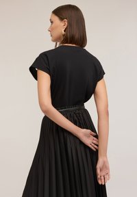 Sort t-shirt med korte opsmøgede ærmer, parret med en plisseret sort nederdel. Nederdelen har en samlede talje for ekstra tekstur.