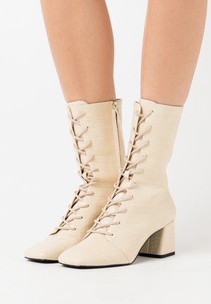 Bottines beige clair à lacets en simili cuir texturé, avec un bout carré et un large talon. Fermeture éclair sur le côté pour un enfilage facile.