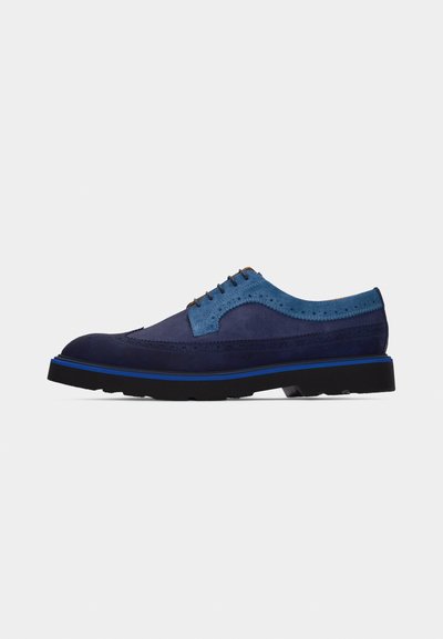 Chaussure Oxford à bout golf en daim bleu foncé pour homme, avec des accents bleu clair et une semelle noire, vue de profil sur fond blanc.