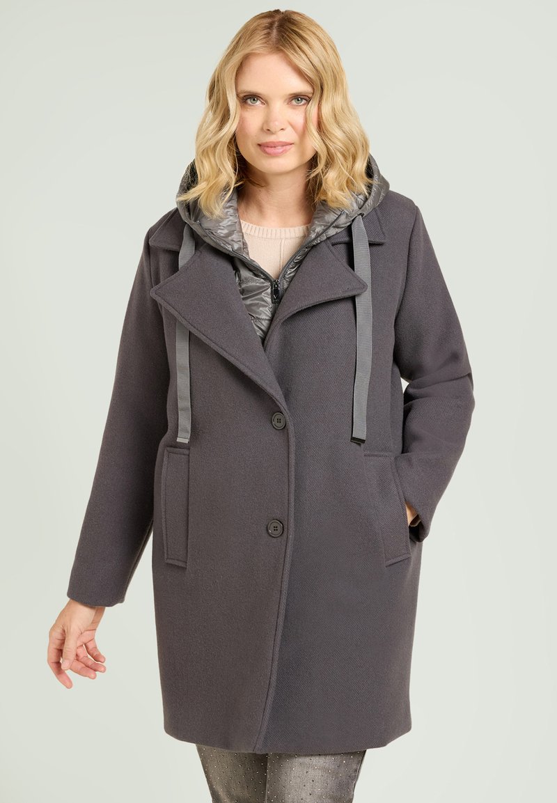 Abrigo gris de mezcla de lana con capucha acolchada, que cuenta con dos bolsillos delanteros, cuello con solapa y cierre de botones. Acabado texturizado y correas ajustables.