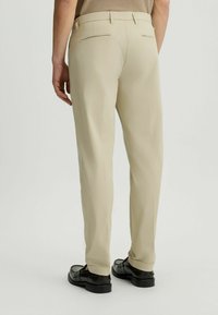 Pantalones beige con corte recto, bolsillos laterales, dos bolsillos traseros y una textura de tela suave. Llevado con zapatos negros.