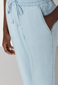 Pantalon léger bleu clair avec taille élastique, cordon de serrage et poches latérales ; texture lisse et coupe décontractée.