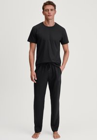 Zwarte korte mouwen t-shirt en bijpassende joggingbroek met trekkoord, beide gemaakt van een gladde stof, met een ontspannen pasvorm en subtiele ontwerpelementen.