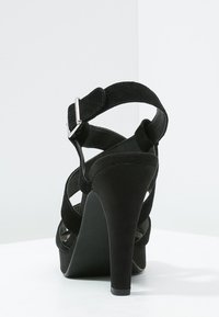 Svart mocka högklackad sandal med flera korsade remmar och spänne. Har en avsmalnande klack och en mjuk textur.