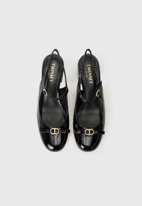 Musta patentoitu keinonahkainen slingback-kengät, joissa on pyöristetty varvas, kultainen solki etuvaljaassa ja pieni korko. Brändin nimi näkyy sisältä.