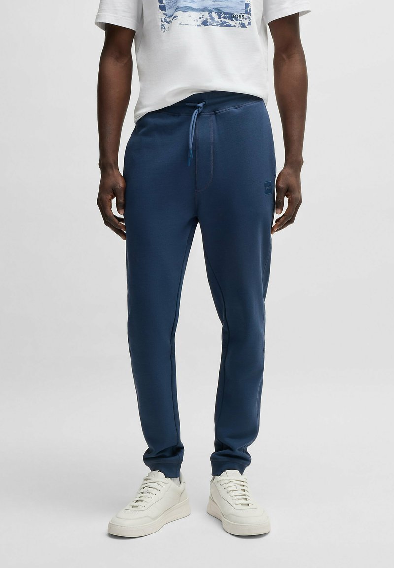 Navy blue sweatpants with elastic waistband and drawstring, tapered leg design, featuring contrasting stitching and a small logo.