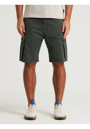 Pantaloni cargo verdi con tasche laterali, realizzati in un tessuto durevole, caratterizzati da una vestibilità comoda e dettagli cuciti. Indossati con sneakers bianche.