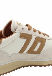 Baskets blanches avec un design en cuir et daim beige, logo "70" bien en vue et semelle en caoutchouc texturé. Les lacets sont marron.