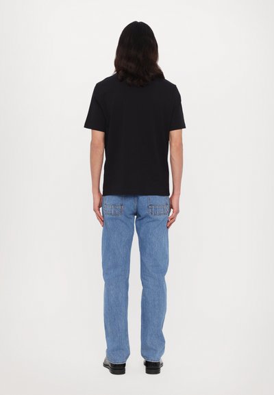 T-shirt noir à manches courtes, jeans bleus à jambe droite avec poches arrière, porté avec des chaussures noires, vu de dos sur fond blanc.