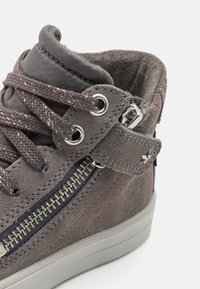 Zapatilla alta de ante gris con costuras rosas, detalle de cremallera plateada y un interior de tejido texturizado. Presenta cordones planos y una correa con hebilla de metal.
