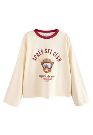 Crèmekleurig shirt met lange mouwen en rode bies, met een skiënd stier als afbeelding en tekst "Après Ski Club Aiguille du Midi Chamonix France est. 1987."