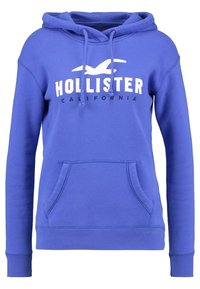 Blå hoodie i bomullsblandning, med framfickor i kengurustil, dragsko på huvan och en stor vit "HOLLISTER CALIFORNIA"-logotyp.