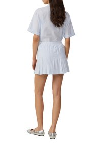 Lichtblauwe blouse met korte mouwen, gecombineerd met een lichtblauwe plissé minirok. Het model draagt zilveren balletschoenen met een zwarte zool.