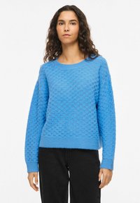 Pull bleu texturé avec un col rond, des manches longues et des poignets et ourlets côtelés. Le tissu présente un motif en forme de bulles.