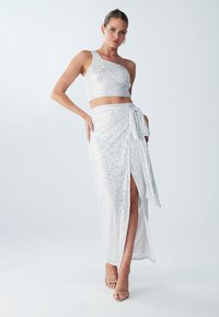 Kjole i to deler med én skulder crop-top og gulvlengde skjørt, begge prydet med glitrende sølvfargede paljetter og en sidelåsing.