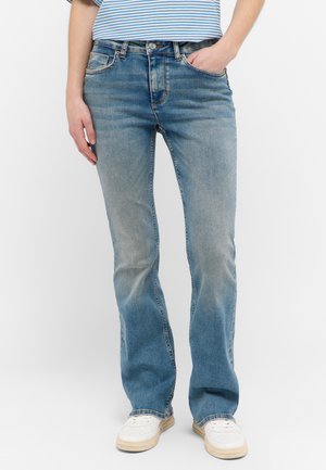 Ljust blå denimjeans med rak bendesign, blekt fram, fem fickor och ett subtilt whiskermönster nära låren. Vita sneakers.