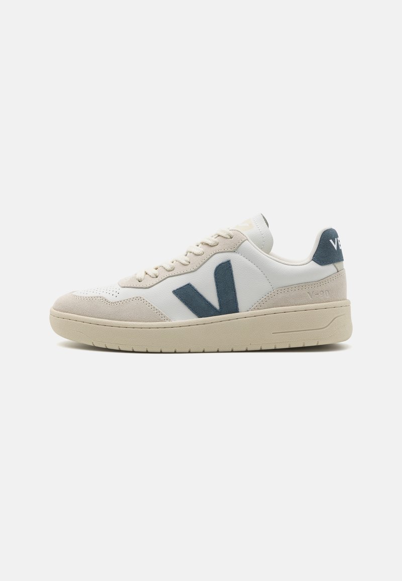 Baskets basses avec semelle beige, dessus en cuir blanc et en daim, et logo "V" gris foncé sur le côté.