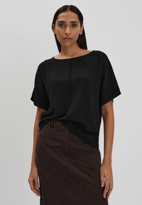 Top nero a maniche corte con vestibilità ampia e scollatura larga. Realizzato in tessuto morbido, abbinato a una gonna a tubino marrone con una texture sottile.