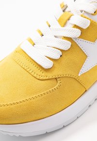Yellow suede sneaker with white thick laces and a stitched white star on the side, featuring a white rubber sole.