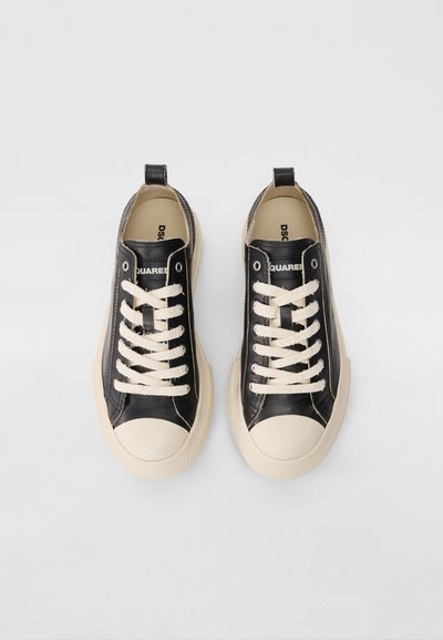 Schwarze Ledersneaker mit cremefarbenen Gummi-Zehenkappen und -sohlen, ausgestattet mit beigen Schnürsenkeln und einer Zuglasche an der Ferse. Markenlogo auf der Schuhzunge sichtbar.