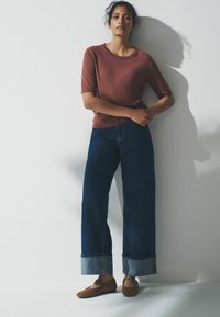 Svetr s krátkými rukávy v rezavé barvě, doplněný širokými tmavými džínami s kontrastním světle modrým lemem. Hnědé baleríny dokončují vzhled.