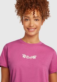 Pink cotton t-shirt with short sleeves, features a white floral logo design on the chest, smooth texture and a relaxed fit.