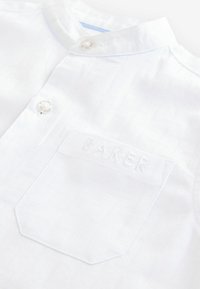 Witte shirt met korte mouwen en een opstaande kraag, uitgerust met een reliëfstructuur, een zak met de tekst "BAKER" en knoopdetails.